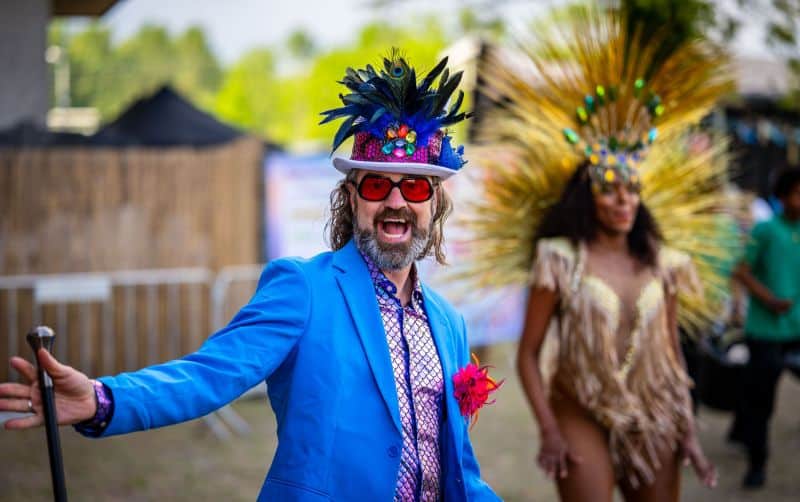 Man in kleurrijk feestkostuum met masker en bril op outdoor festival.