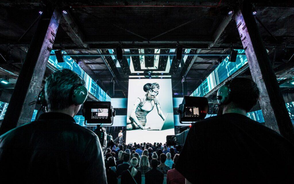 Hackathon evenement met deelnemers en grote schermpresentatie.